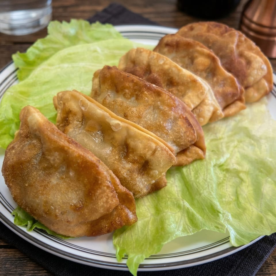 Golden-brown fried dumplings, arranged on a bed of fresh green lettuce on a white plate.