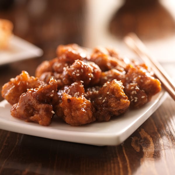 Close-up of sesame chicken with a sweet and savory glaze, served on a white plate with chopsticks.