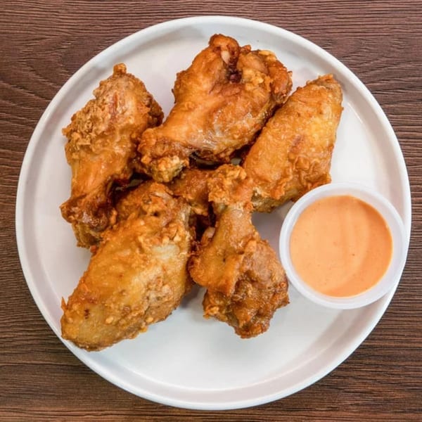 Crispy fried chicken wings on a white plate with a side of orange dipping sauce.