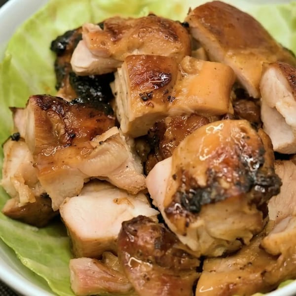 Close-up of diced grilled chicken with a glossy glaze, served on a bed of green lettuce.