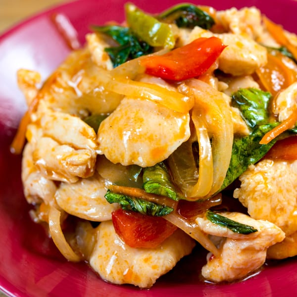 Close-up of stir-fried chicken with bell peppers, onions, and basil in a savory sauce.
